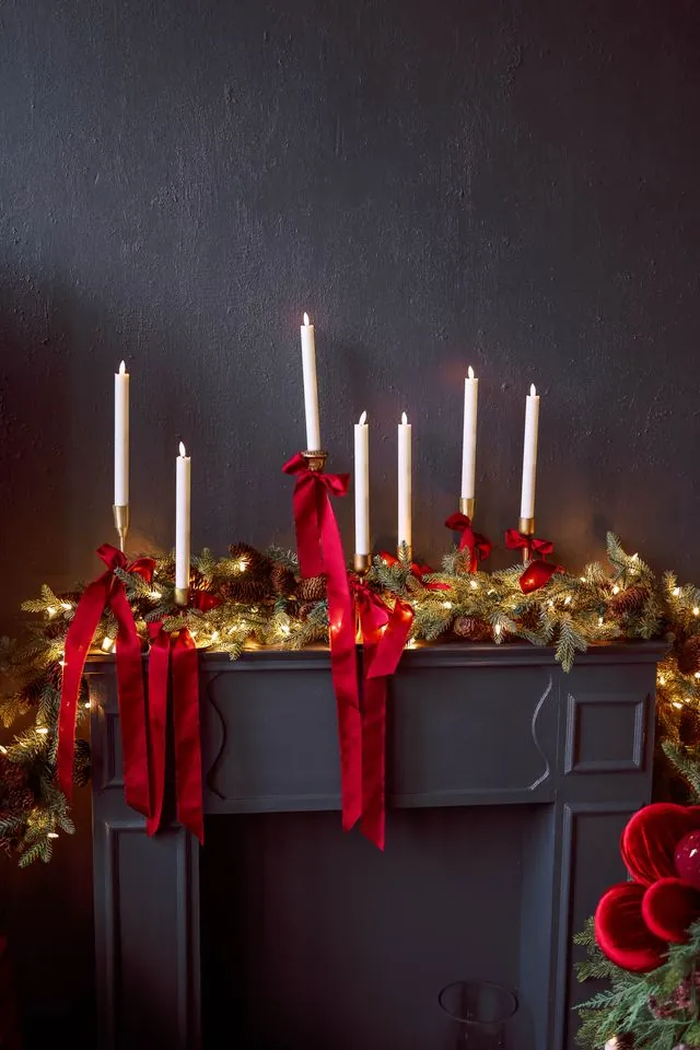 Dark mantel with a pine garland, burgundy velvet ribbon and white taper candles