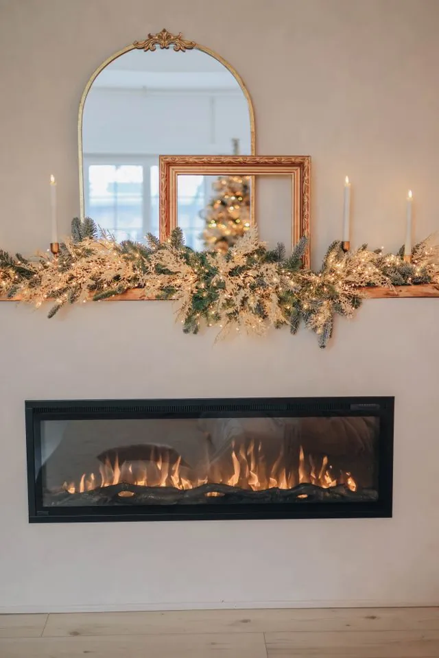 Arched gilt mirror leaning above a fireplace, framed by a lush garland