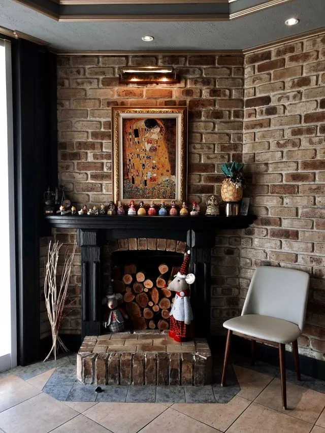 Vintage painting hung above a corner brick fireplace with stacked firewood