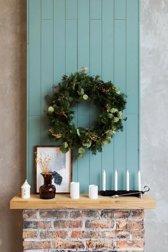 Simple mantel without garland: a wreath, white candles and a small vase on a wooden shelf