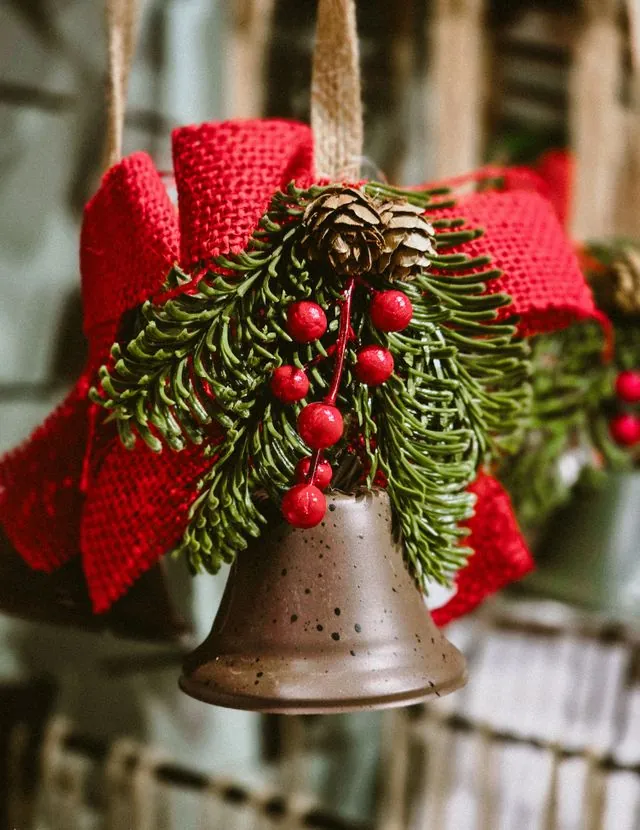 Rustic brass bell with red ribbon, pine and berries hanging from a garland