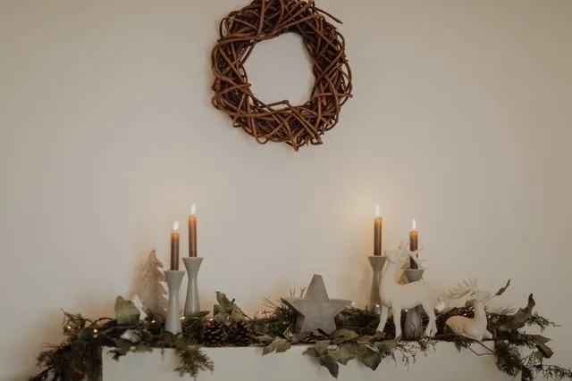 Wall shelf styled like a Christmas mantel with a twig wreath, candles and greenery