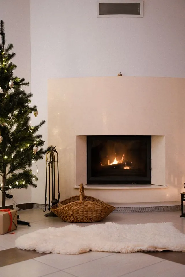Simple white fireplace with a lit fire and a Christmas tree on one side