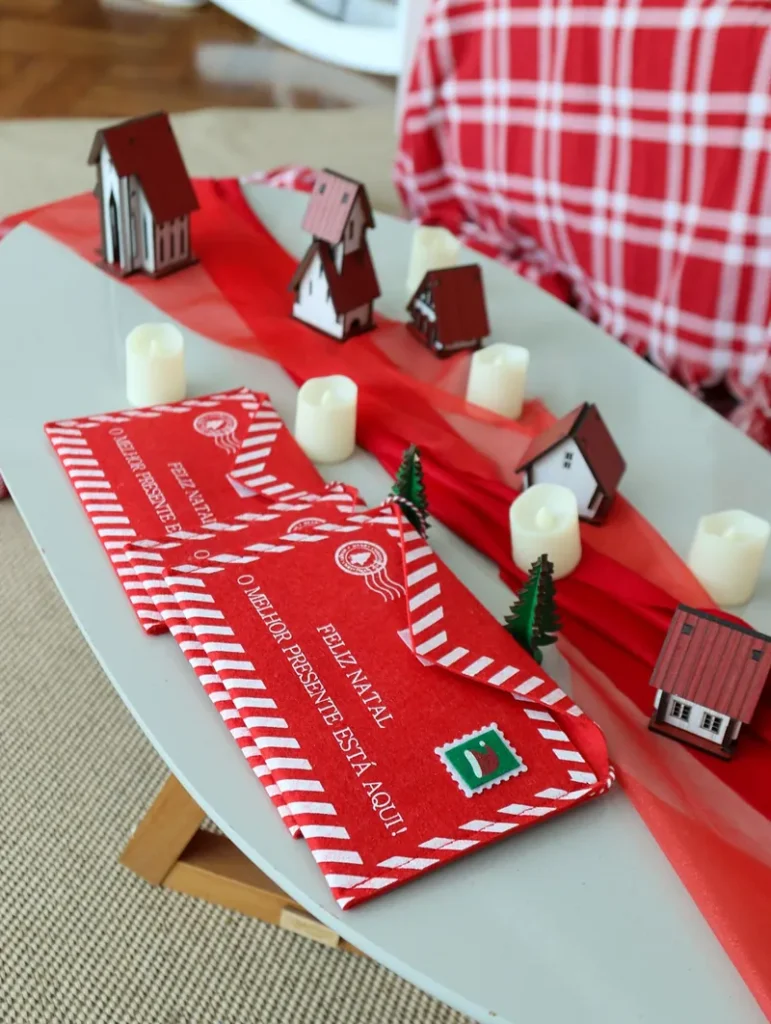 Red Christmas letter envelopes with candles and tiny red houses on a table, a christmas cash envelope system for the envelope split