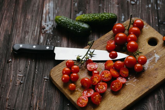 Sharp chef's knife on a cutting board with cherry tomatoes and cucumbers, one good kitchen knife as a gift