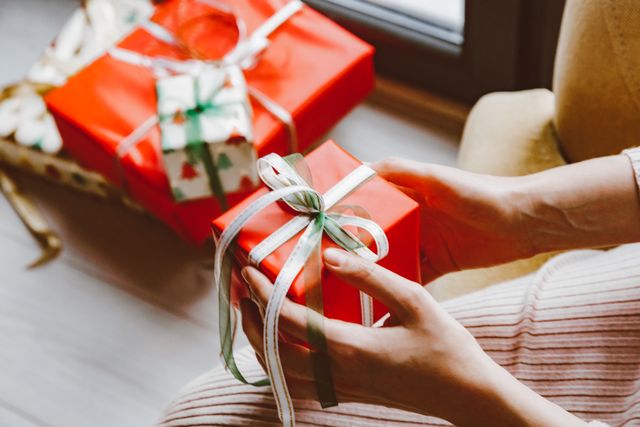 Hands holding a red wrapped Christmas gift with a white ribbon, minimalist christmas gift ideas for women