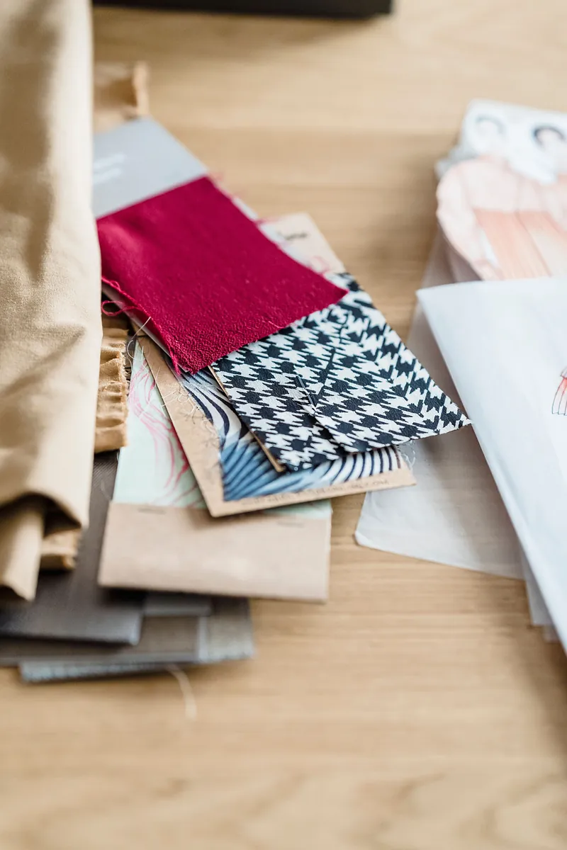 Burgundy fabric swatch next to houndstooth and neutral fabric samples on a wooden desk, color pairs for a burgundy sweater