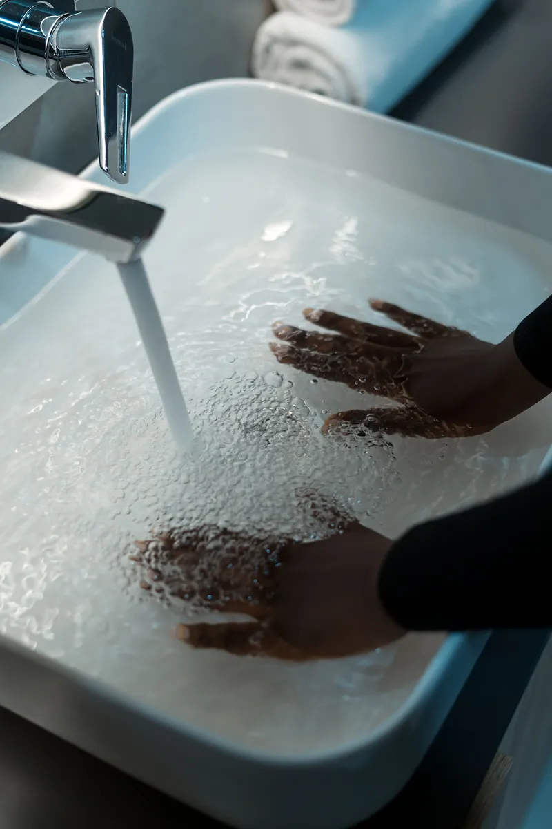 Hands in a white basin of lukewarm water running from a tap, ready to hand wash a wool sweater